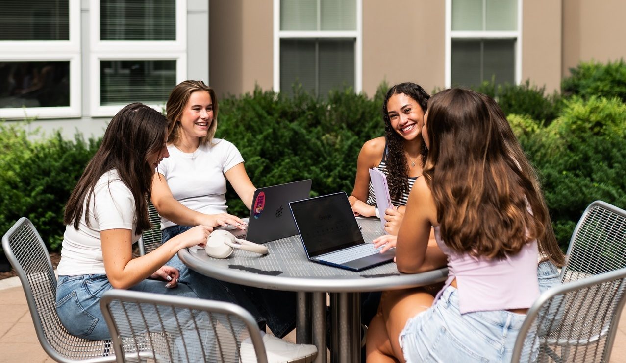 four girls sitting and smiling while studying outside at landmark college park