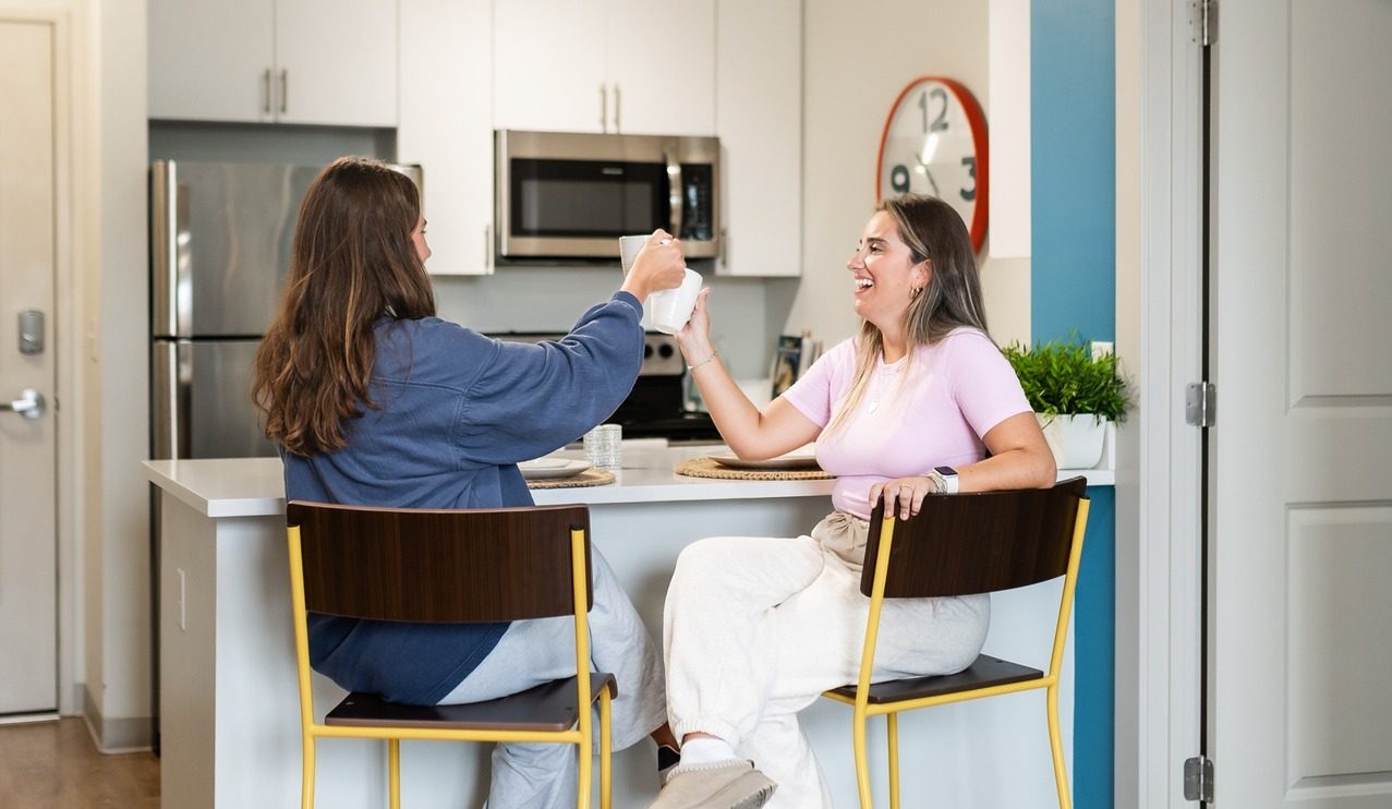 two girls sitting at landmark college park apartment cheering and laughing