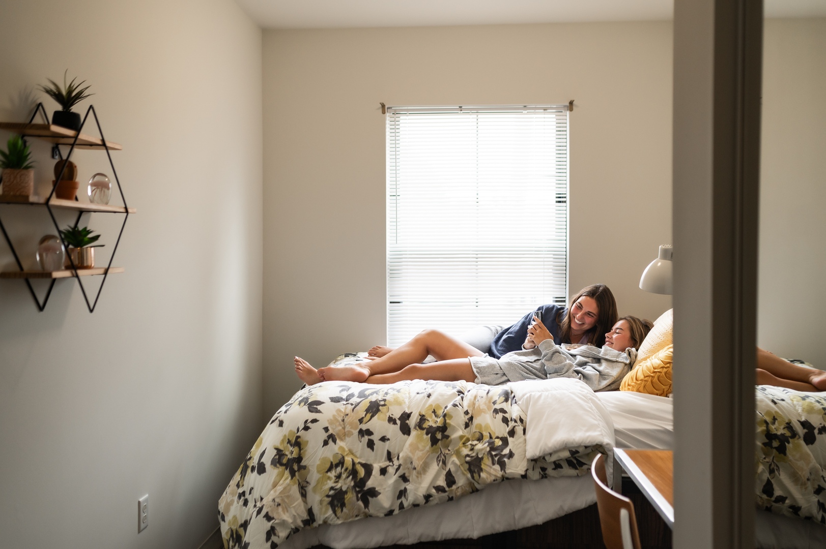 two girls laying down laughing about something over the phone in their bedroom at landmark college park