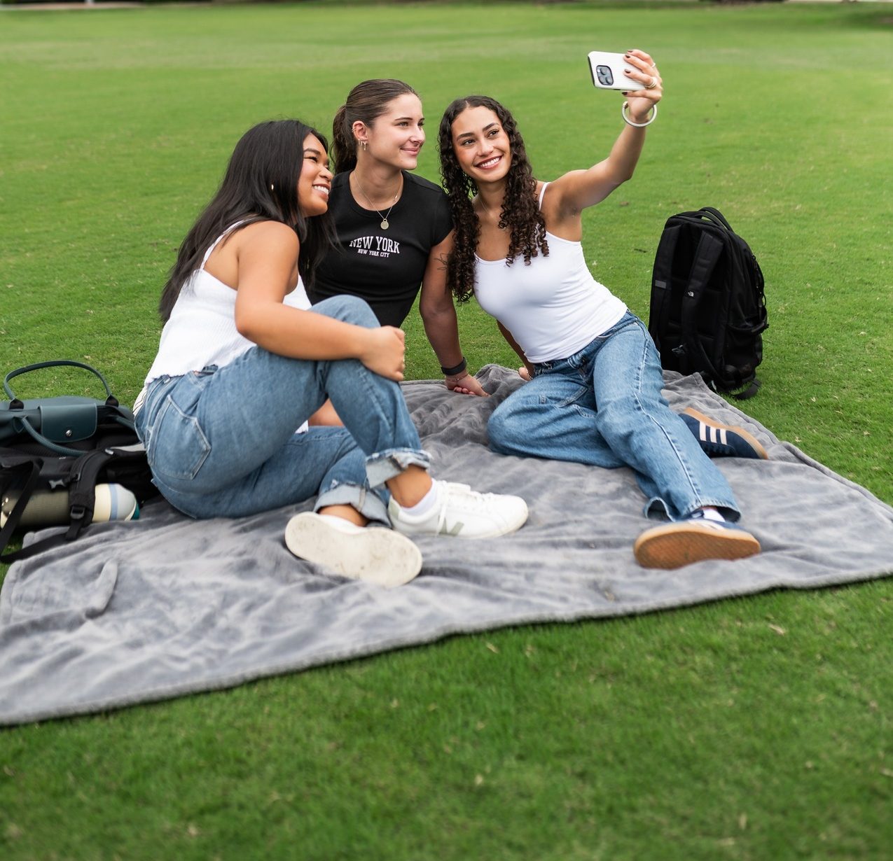 three girls taking a picture on a picnic blanket outside on a grass field